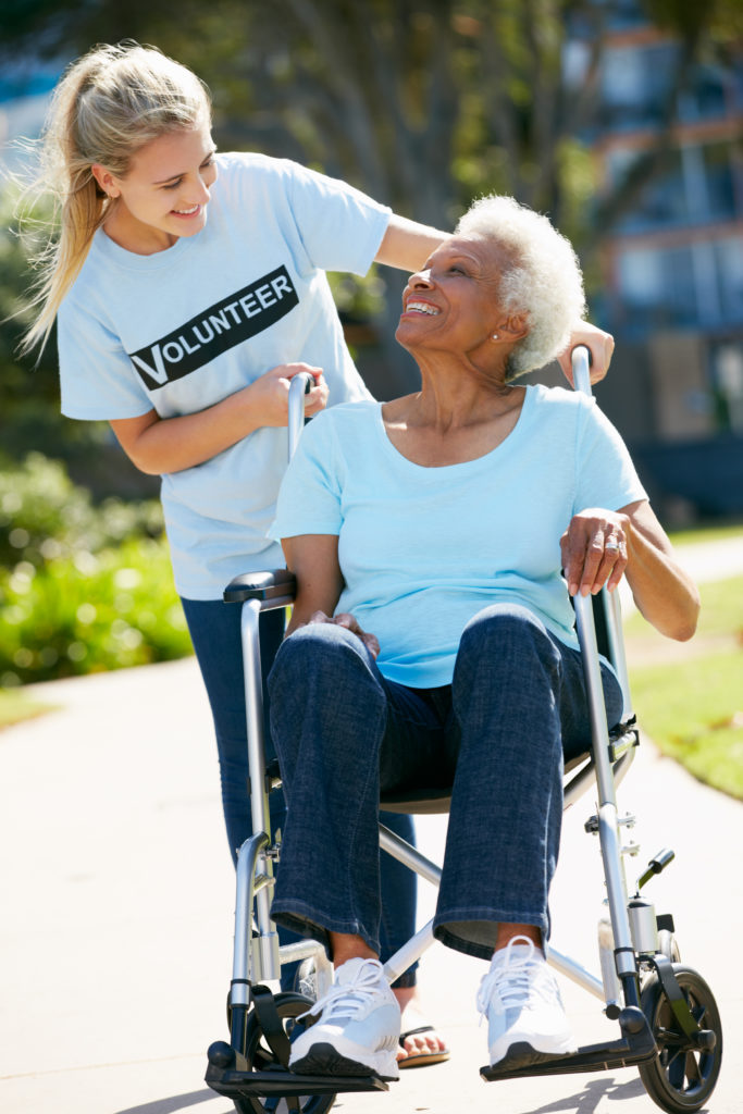 A teenage volunteer pushing a wheelchair of a senior woman Volunteer